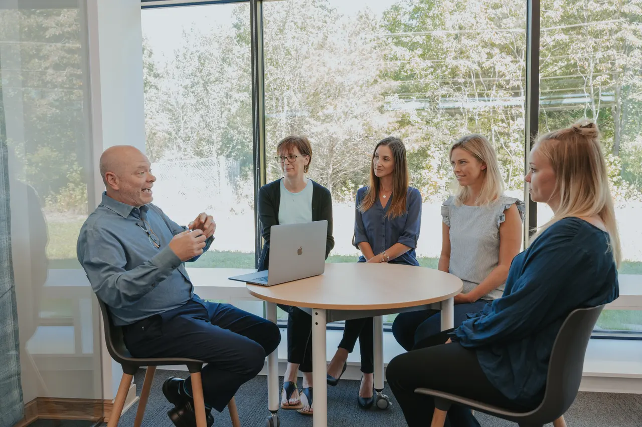 Patrick talking with four colleagues around a table by the windows.