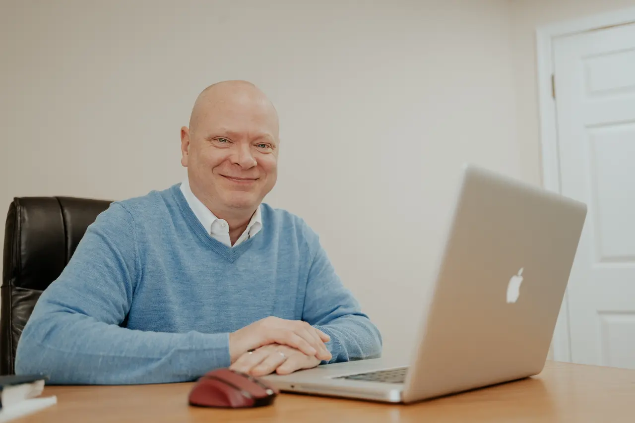 Patrick Lee seated at his desk, smiling beside his laptop.