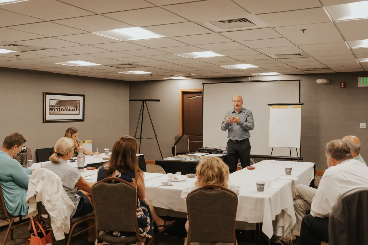 Patrick leading a workshop with participants seated around conference tables.